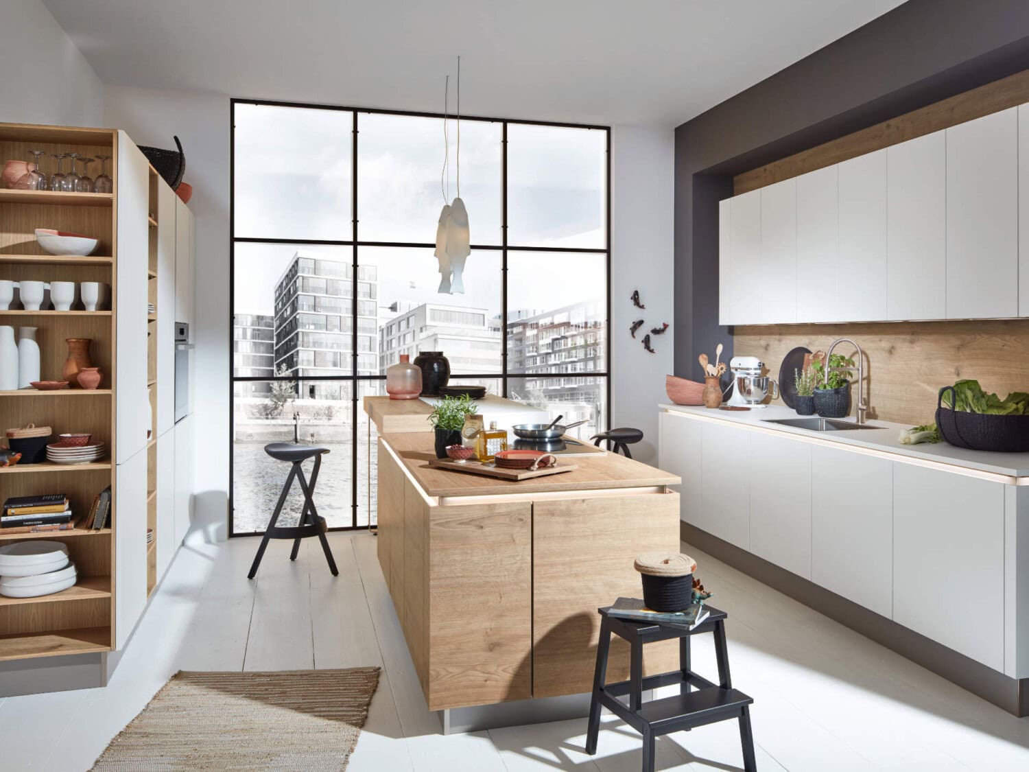 Moderner Küchenraum mit weißer Schrankfront, hölzerner Kücheninsel und großem Fenster mit Stadtblick, stilvolle Dekorationen und Küchenutensilien für ein modernes Wohngefühl.