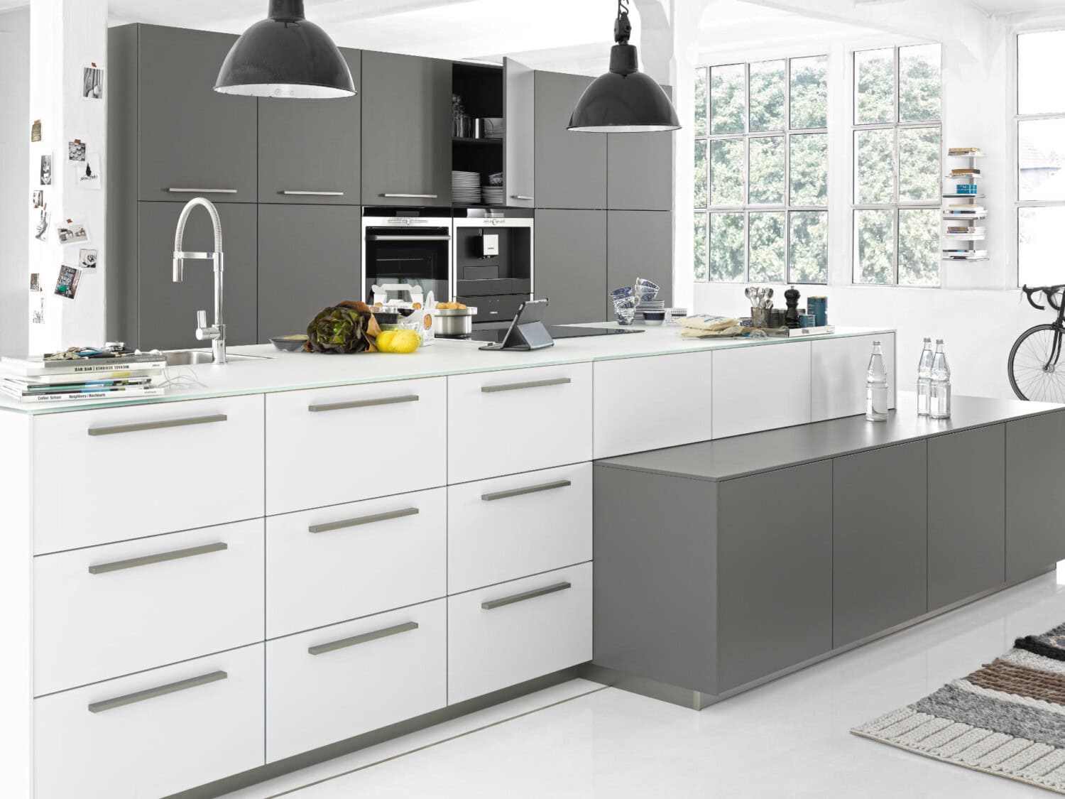 Moderne Küchenzeile mit weißem und grauem Design, große Fenster und stilvolle Küchenutensilien für ein attraktives Küchenambiente.