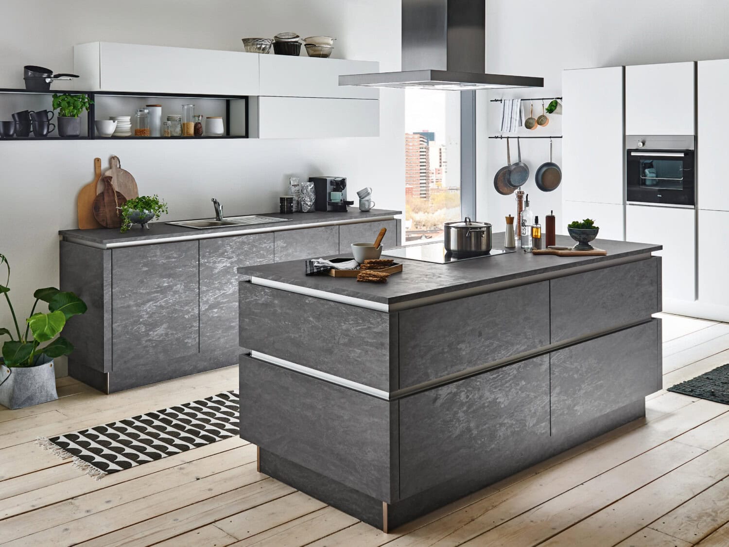 Elegante moderne Landhausküche mit grauem Naturstein und weißen Hochglanzfronten, viel Stauraum, offene Wandregale, große Fenster mit Stadtblick, Holzfußboden, stilvolle Küchenutensilien und Pflanzen.